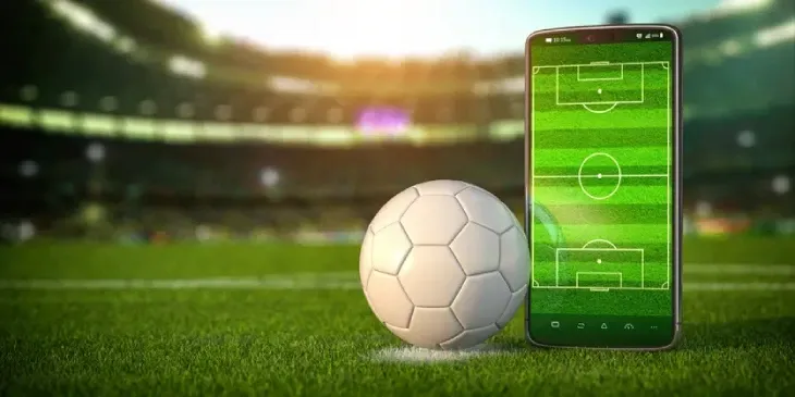 Bola de futebol ao lado de um celular com campo na tela, num estádio, ilustrando o app Futebol da Hora 3.7