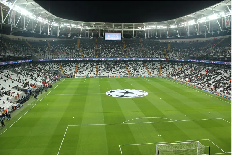 Estádio iluminado à noite com o logotipo da Champions League no centro do gramado antes de uma partida